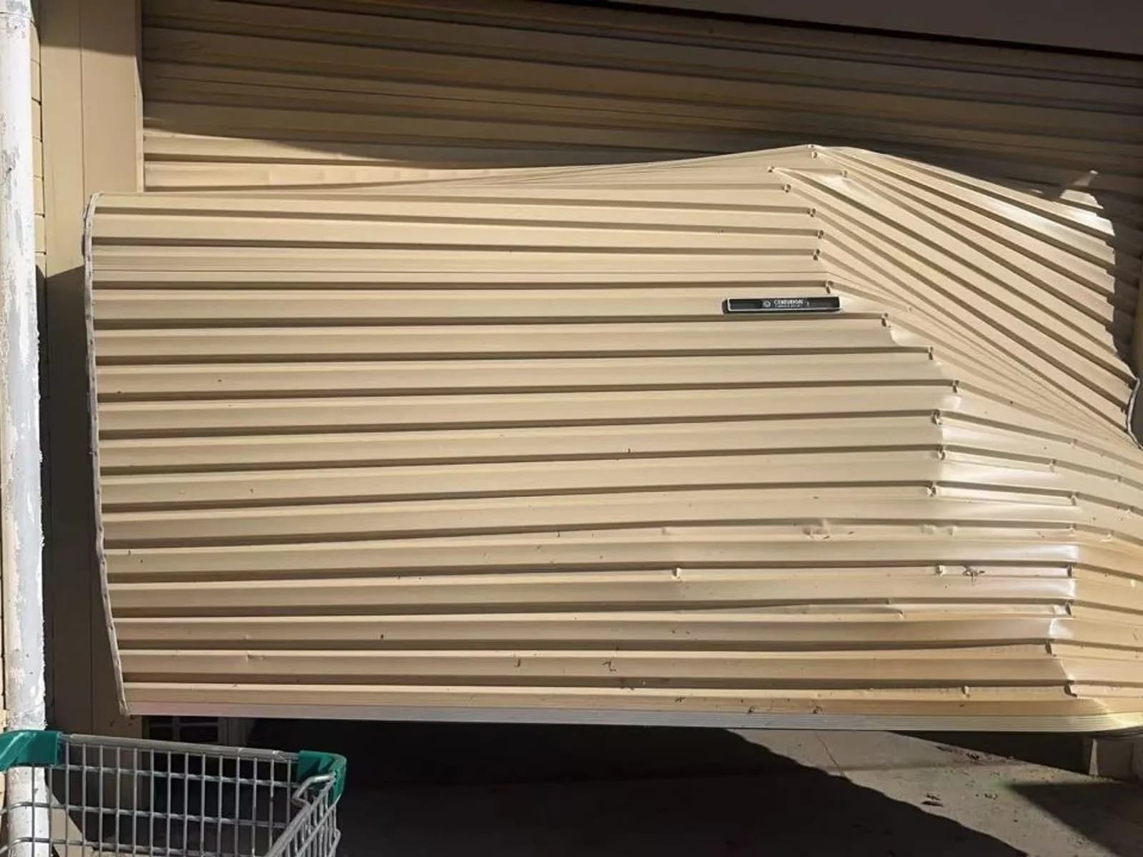 Roller door curtain buckled and creased across several corrugations after an impact, seen from the driveway Roller door curtain buckled and creased across several corrugations after an impact, seen from the driveway