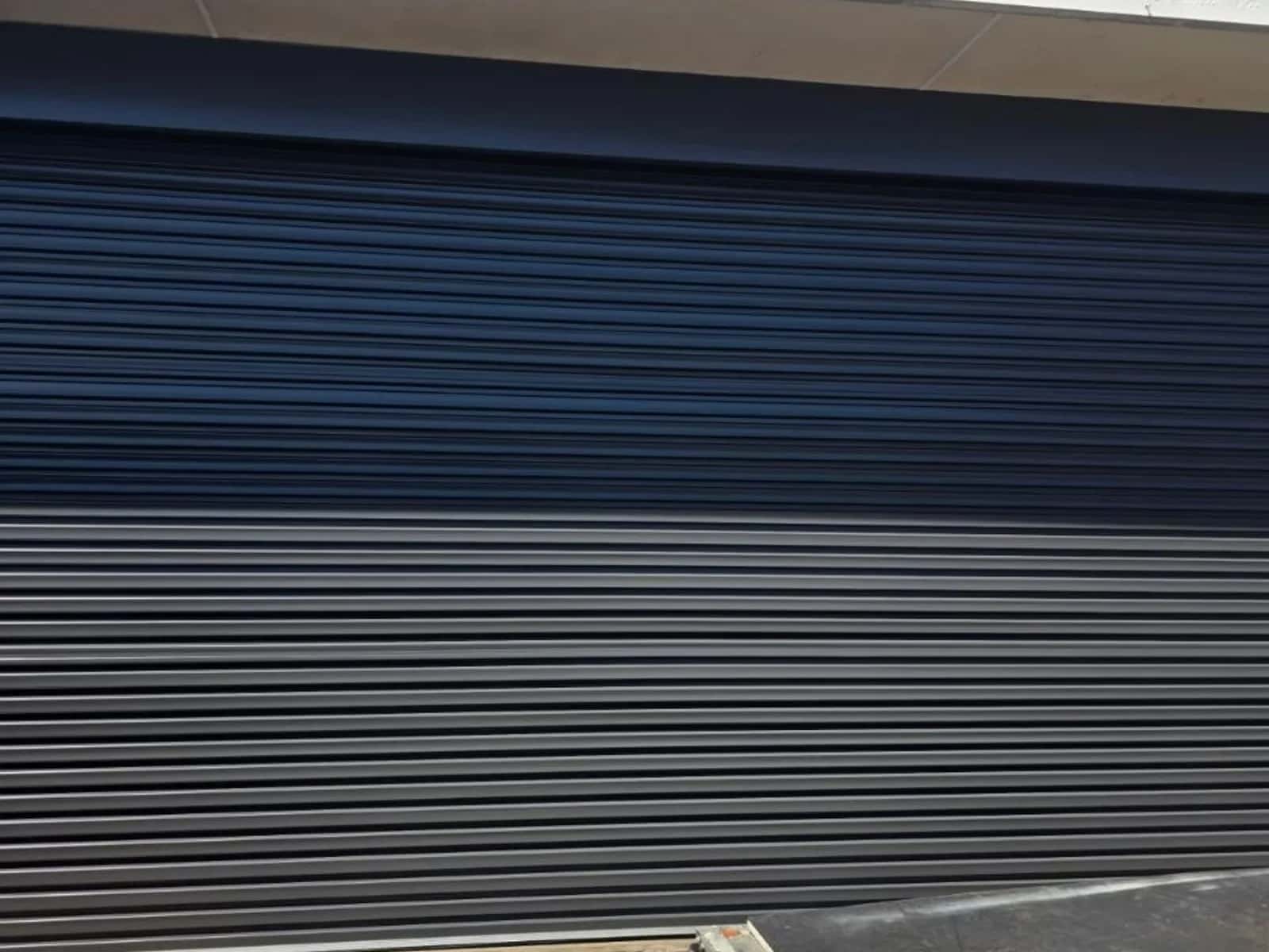 Charcoal commercial roller shutter closed across a shopfront opening, curtain slats seated in the side guides