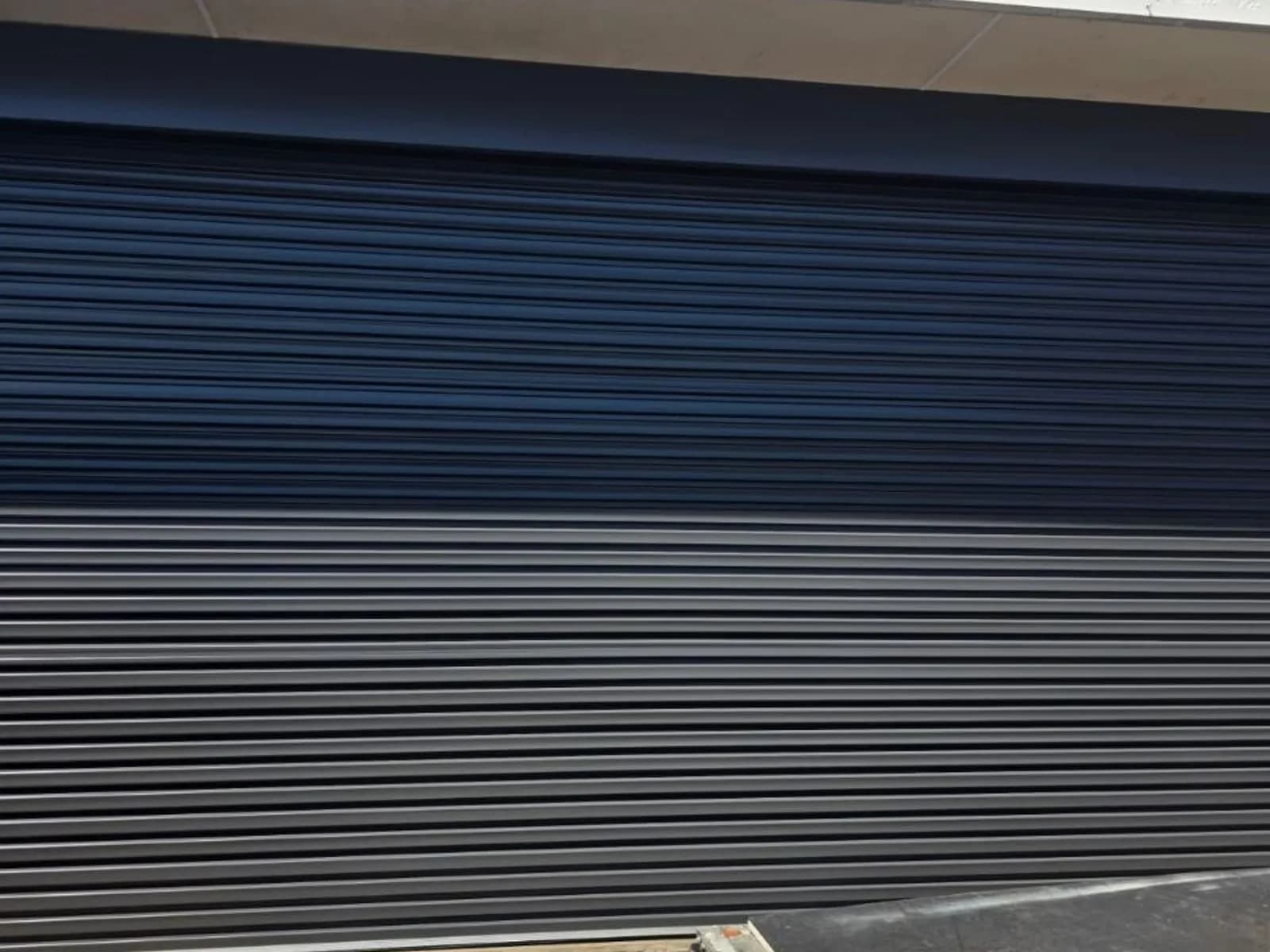 Charcoal commercial roller shutter closed across a shopfront opening, curtain slats seated in the side guides Charcoal commercial roller shutter closed across a shopfront opening, curtain slats seated in the side guides
