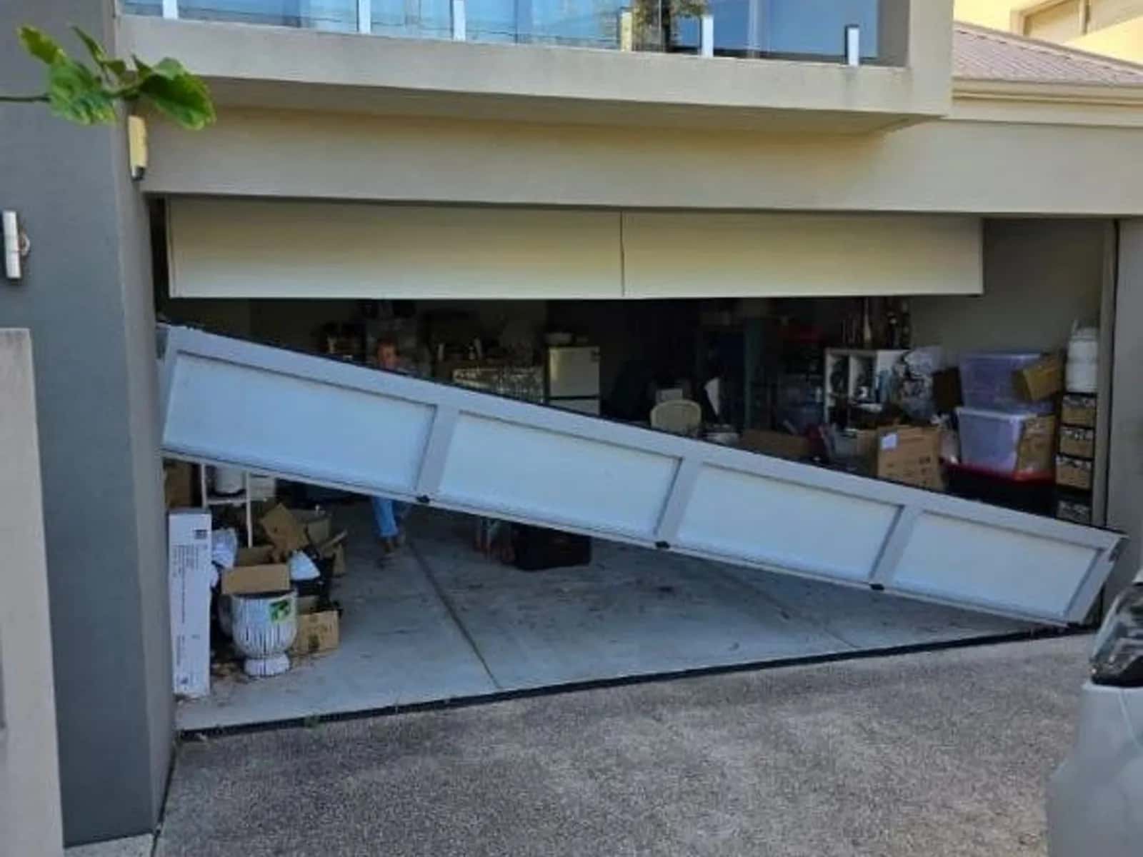 Collapsed sectional garage door with its panels dropped and sitting crooked in the opening, before repair