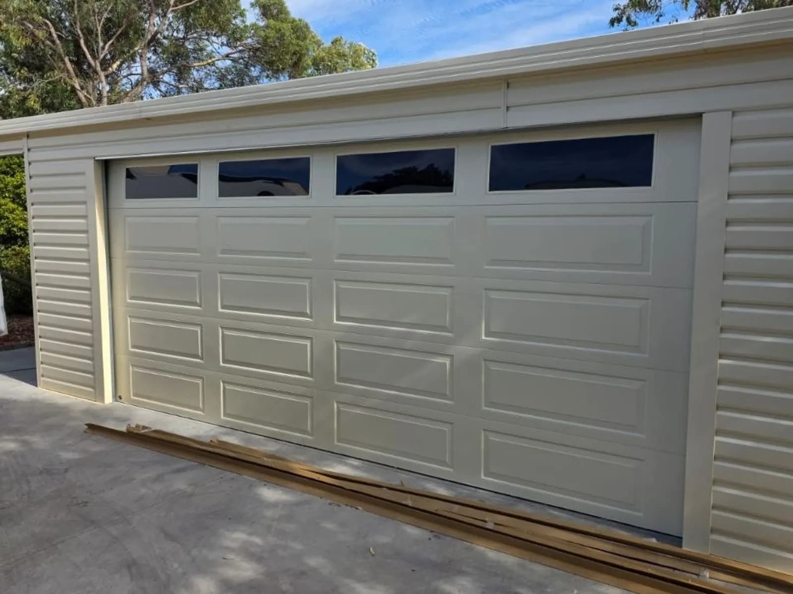 Cream panel-lift sectional garage door with raised pressings and a row of window inserts on a brick home