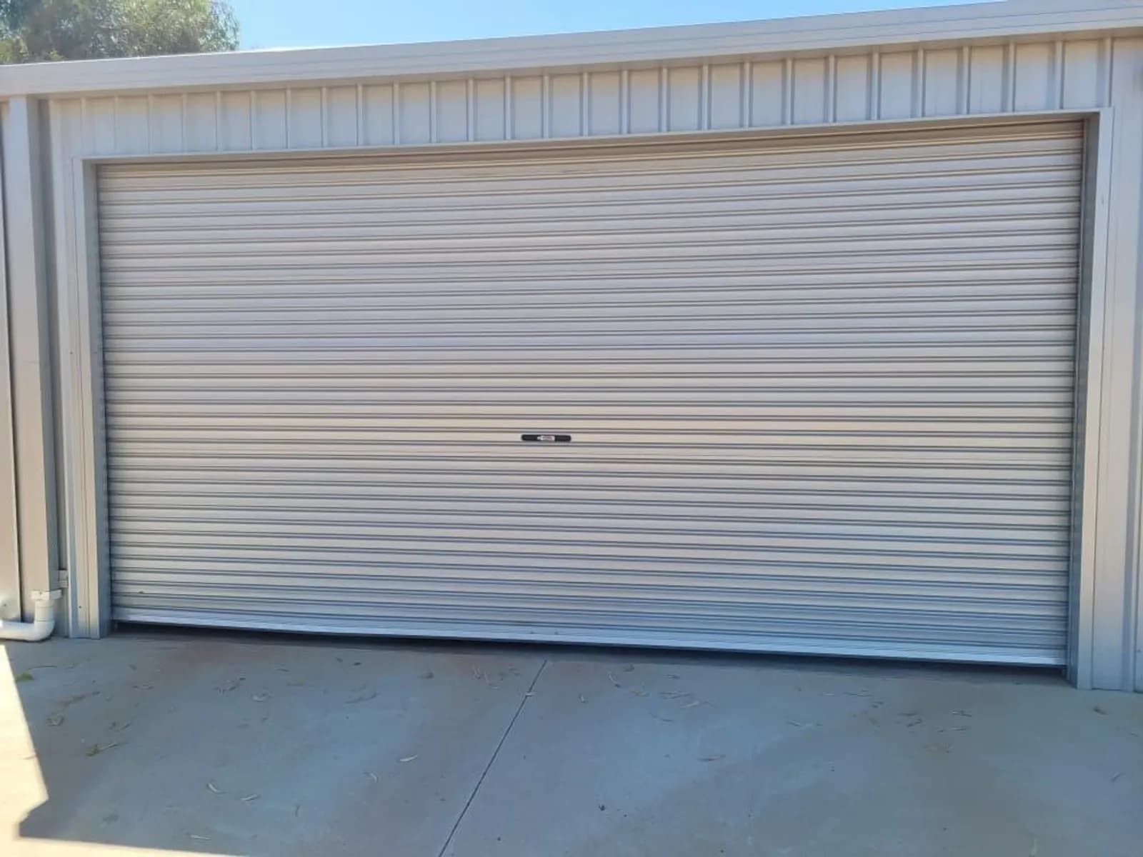 Cream Colorbond roller door closed on a shed, the curtain rolled onto its drum above the opening