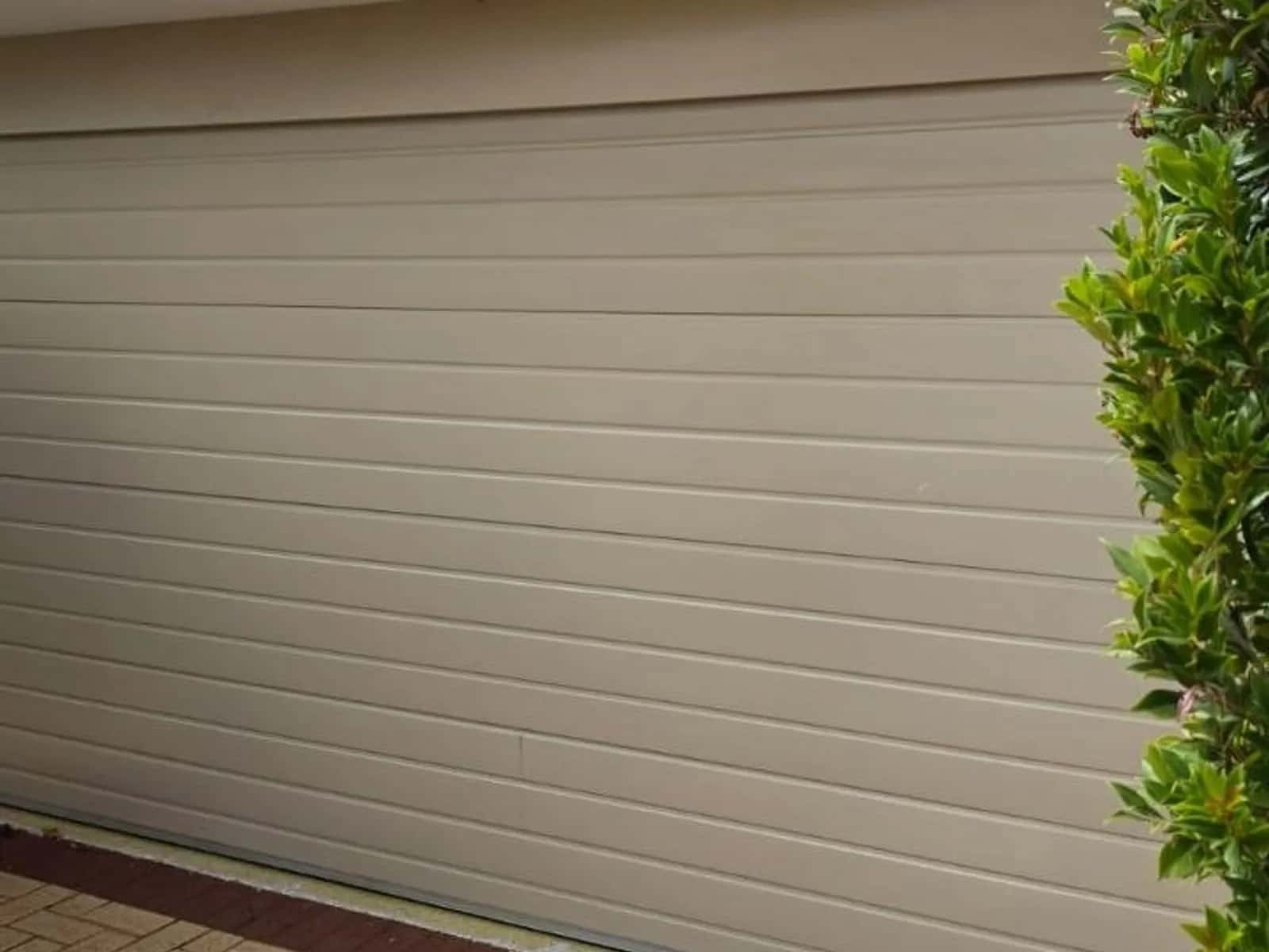 Cream ribbed steel roller door, closed, beside a clipped hedge on a paved driveway