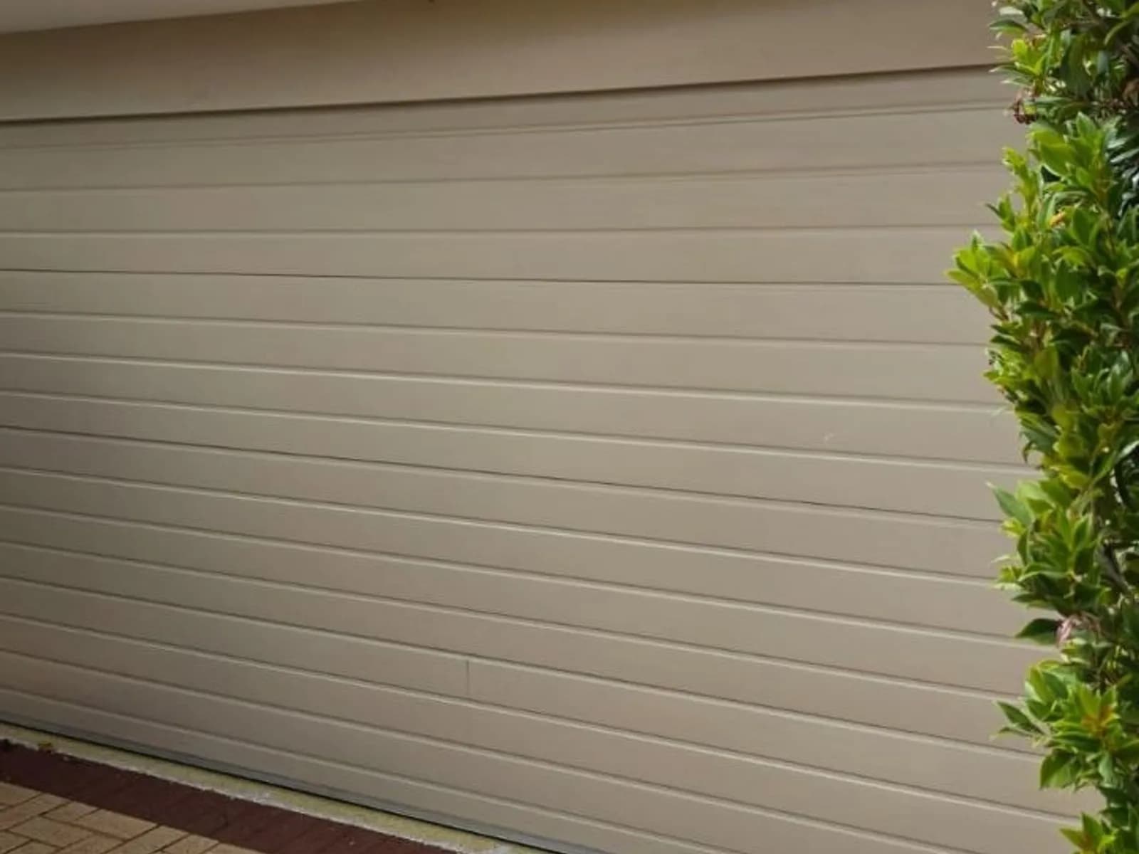 Cream roller door closed on a concrete driveway, its bottom rail resting on the slab where the bottom seal sits