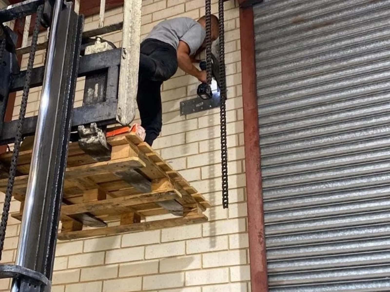 Technician servicing a roller shutter motor unit mounted beside the door's drum