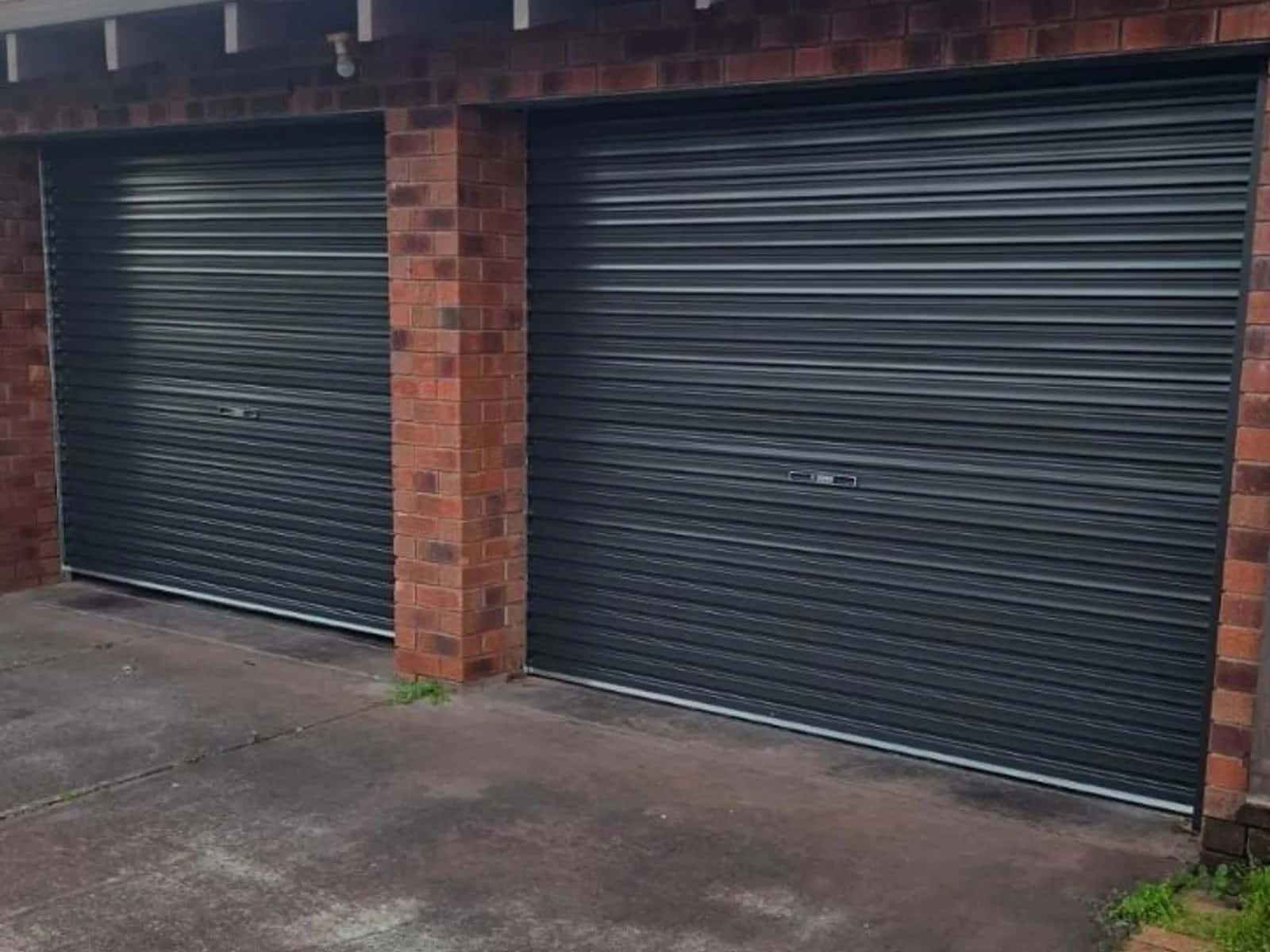 Two Monument grey Colorbond roller doors side by side on a red brick double garage