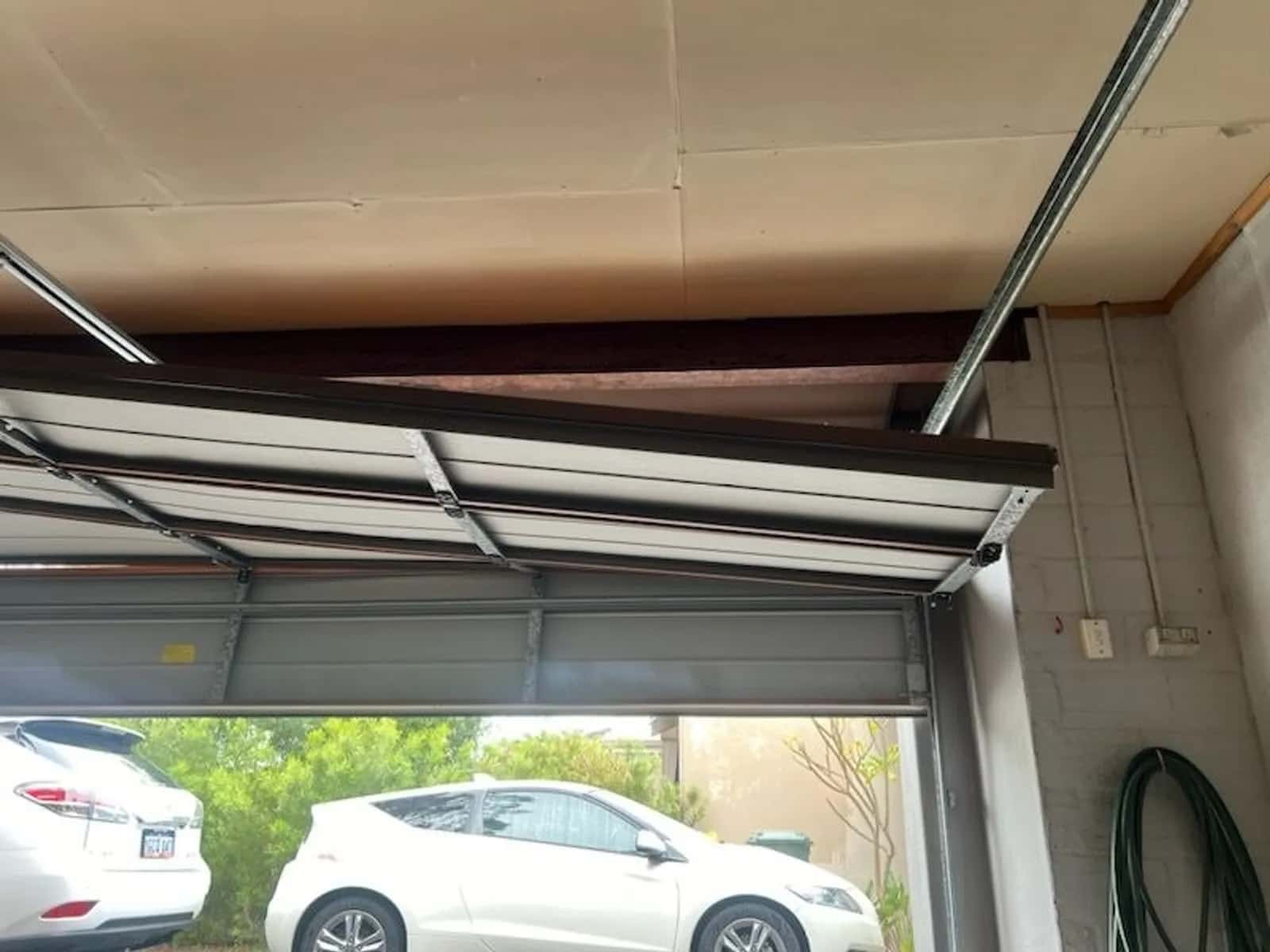 Sectional garage door sitting crooked in its opening, one panel pulled clear of the track on the low side