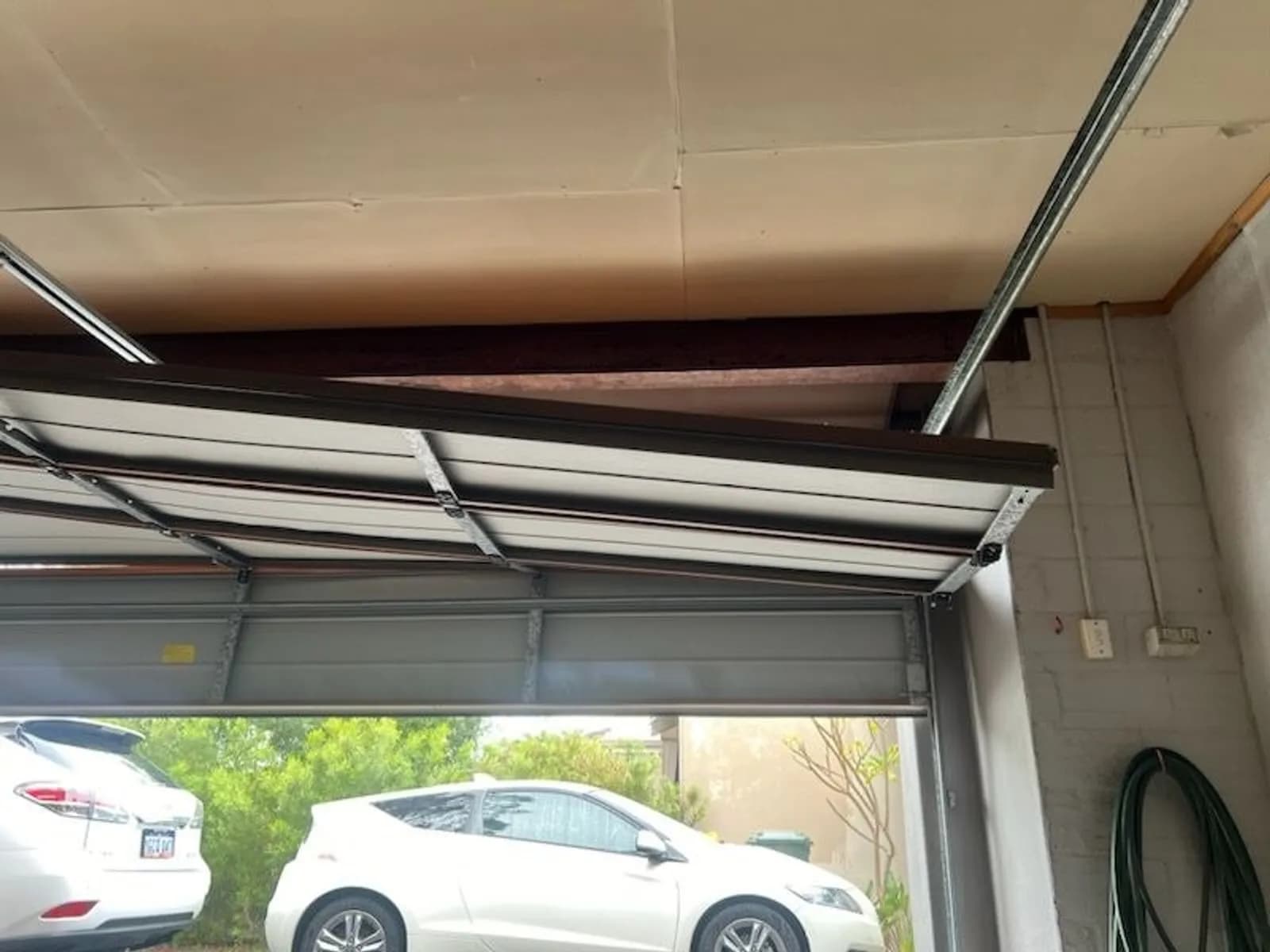 Sectional garage door sitting crooked in its opening, one panel pulled clear of the track on the low side Sectional garage door sitting crooked in its opening, one panel pulled clear of the track on the low side