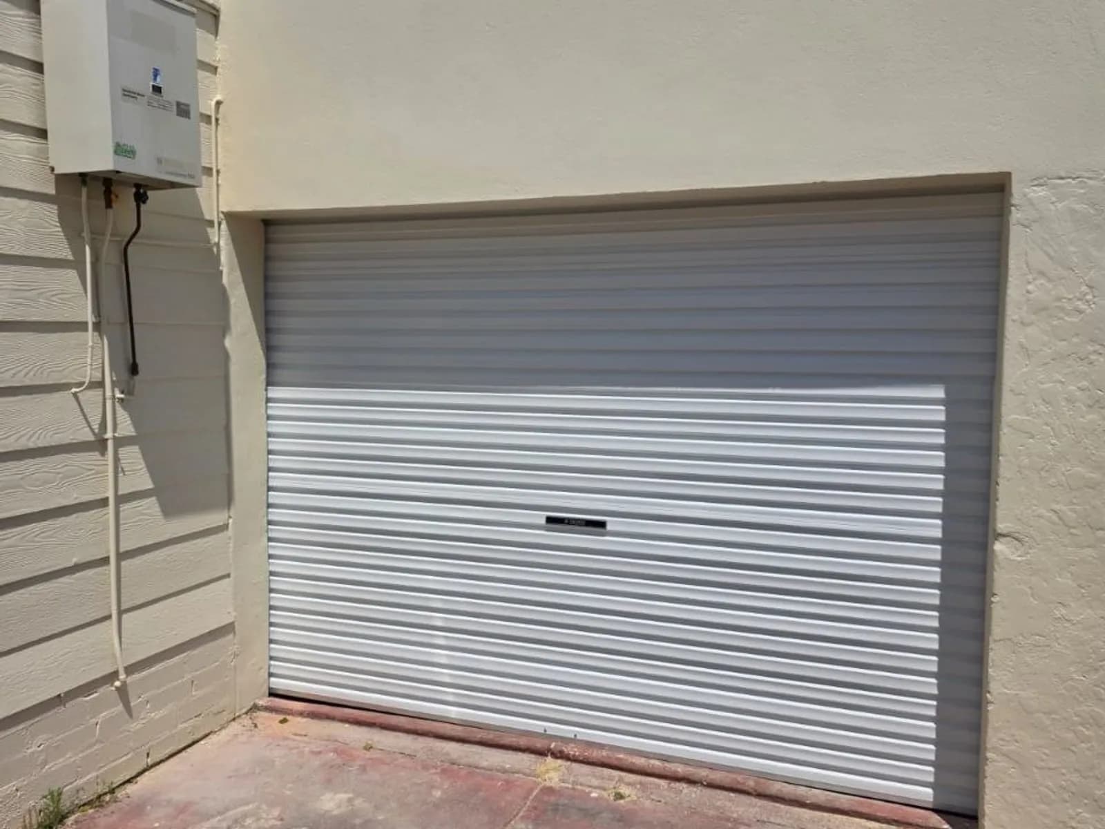 White Steel-Line roller door set into a rendered garage wall, with the opener fitted at one end of the curtain roll