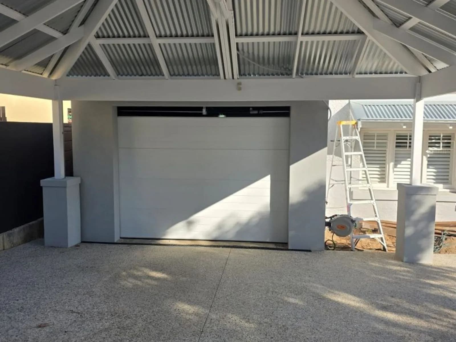 White sectional garage door under a white exposed-truss gable roof in Applecross, with an aggregate driveway in front